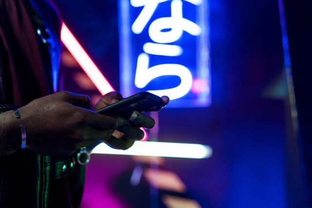 Hands holding a smartphone against neon city lights at night